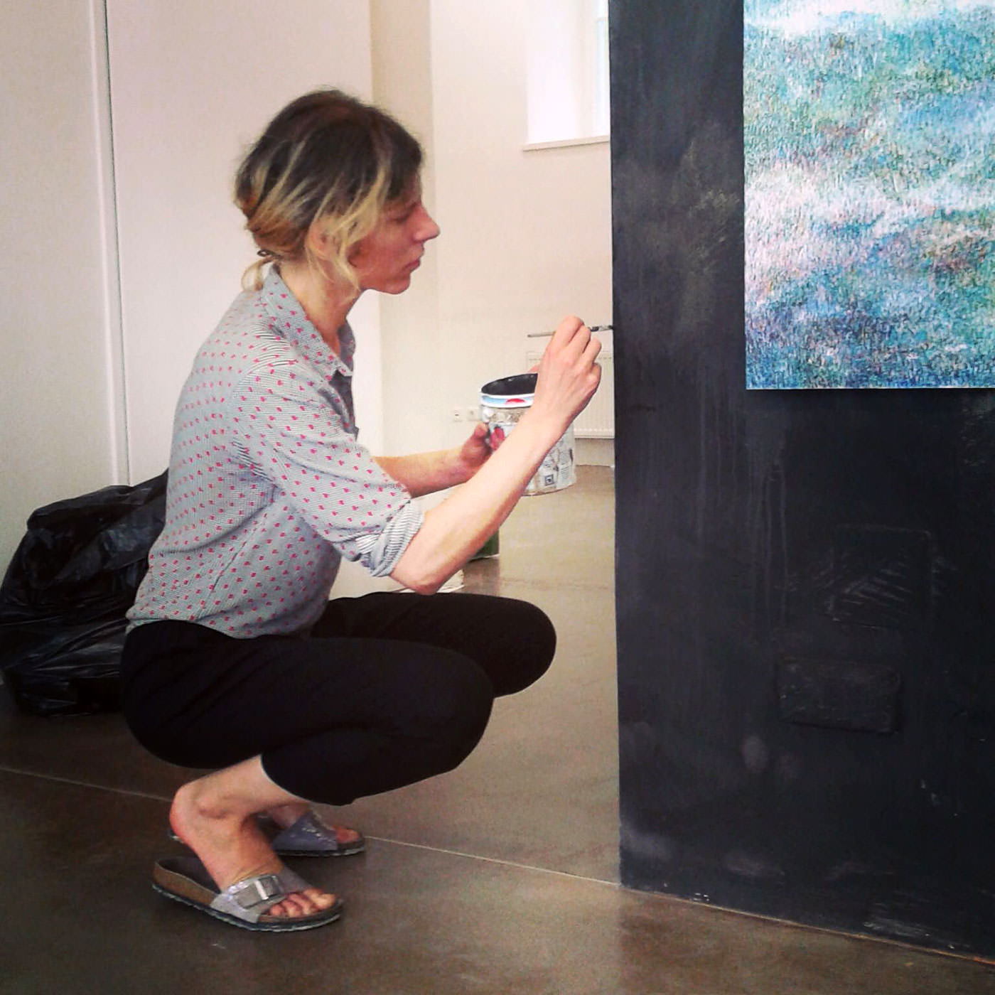 Linda Berger in Seitenansicht, hockend mit Pinsel in der Hand, konzentriert an einer Wand malend.
