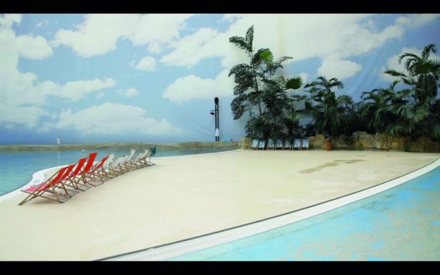 Filmstill Strandansicht mit Palmen, Meer und Liegenstühlen