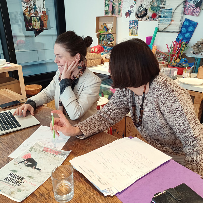 Julia Hartmann und Maria C. Holter sitzen an einem Arbeitstisch mit Computer und SChriftstücken